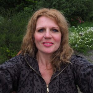Frau mit natürlicher Schönheit im Freien, umgeben von Pflanzen und Blumen.